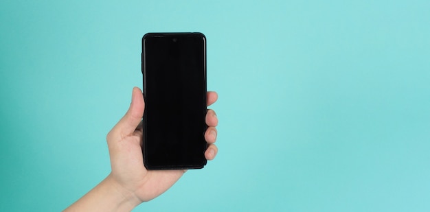 Hand holding mobile phone on green mint background.