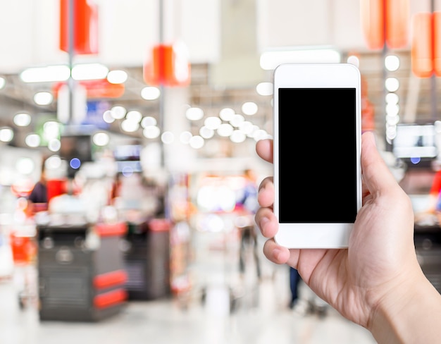 Foto passi il telefono cellulare della tenuta con il cliente della sfuocatura al fondo del deposito del supermercato