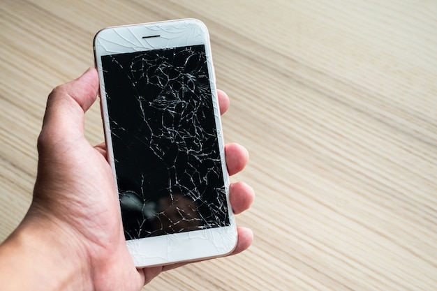 Hand holding mobile phone with broken glass screen