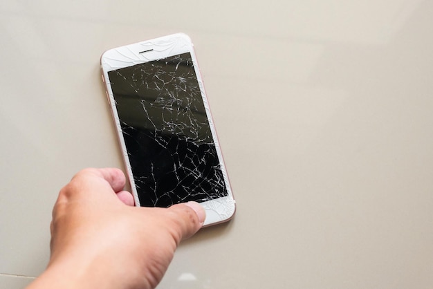 Hand holding mobile phone with broken glass screen