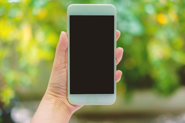 Hand holding mobile smartphone on blurred natural green background