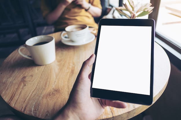 Hand holding mock up tablet pc in cafe with people