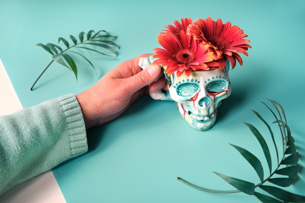 Hand holding mug shaped as skull with gerbera