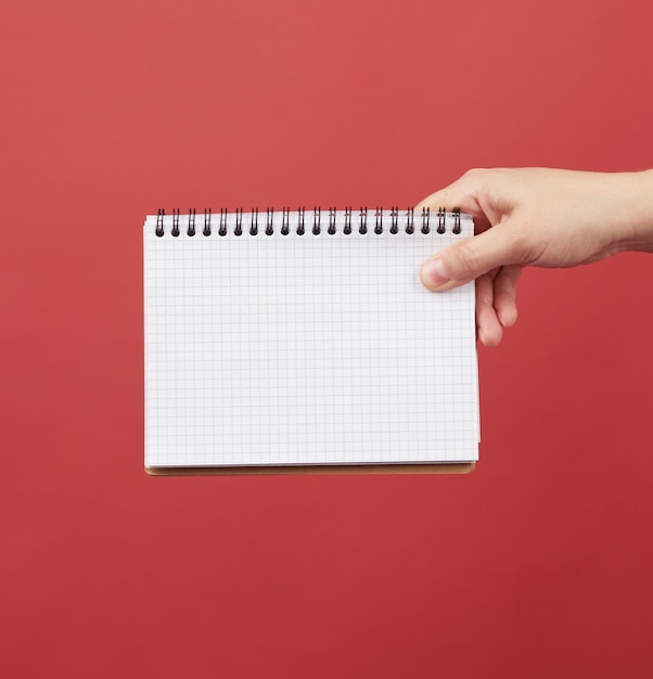 Hand holding an open spiral notebook with empty white sheets