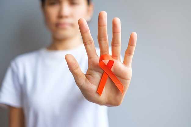 Hand holding Orange Ribbon for Leukemia, Kidney cancer day, world Multiple Sclerosis, CRPS, Self Injury Awareness month. Healthcare and word cancer day concept