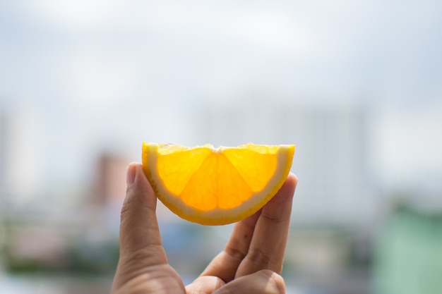 Hand holding orange slice with sky. soft focus.