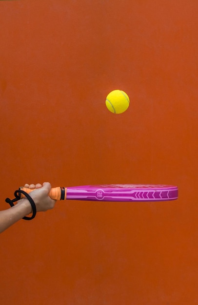 Hand Holding A Paddle Tennis Racket Hitting The Ball On An Orange Background.Sports