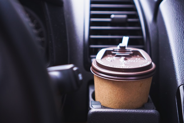 Hand holding paper coffee cup while driving a car in the morning