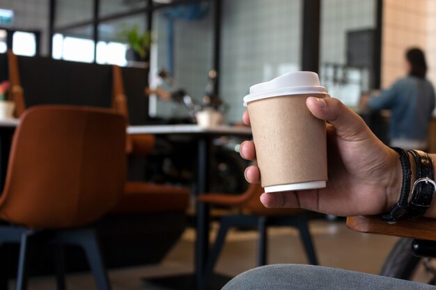 hand holding paper cup of coffee in cafe 