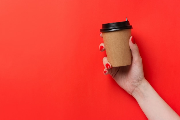 Passi la tazza di caffè di carta della tenuta su fondo rosso.