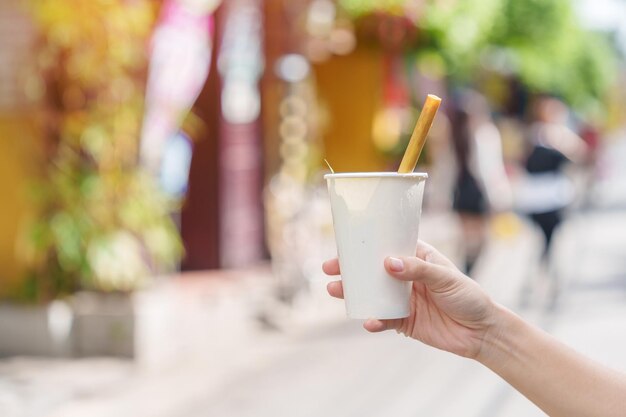 蓮の花びらと茶葉を入れたハーブドリンクの紙コップを持つ手は、ベトナム中部のホイアンの古代の町で観光客に最も人気のある飲み物です