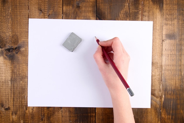 Photo hand holding pencil and erase with paper on wooden