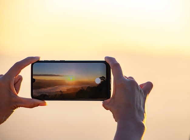 Photo hand holding the phone shooting the morning sun and the fog.