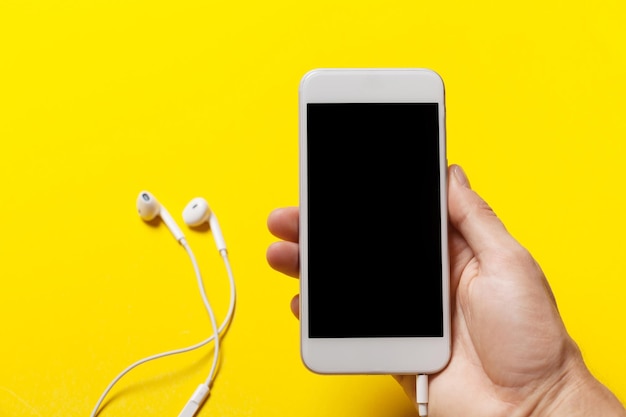 Hand holding phone with headphone on a yellow background clipping path inside