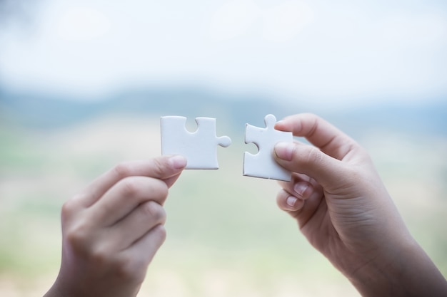 Hand holding piece of blank jigsaw puzzle with nature background.