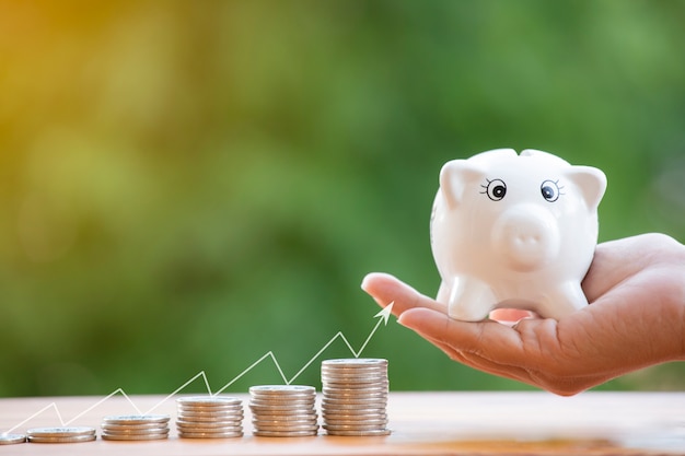 Hand holding a piggy bank next to a collection of coins