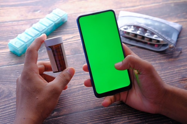 Hand holding pill container and smart phone on table