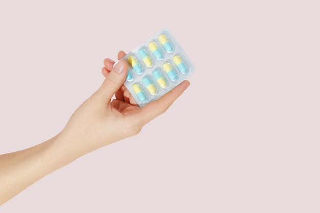 Hand holding pills in blister packs on a pink background Health care concept