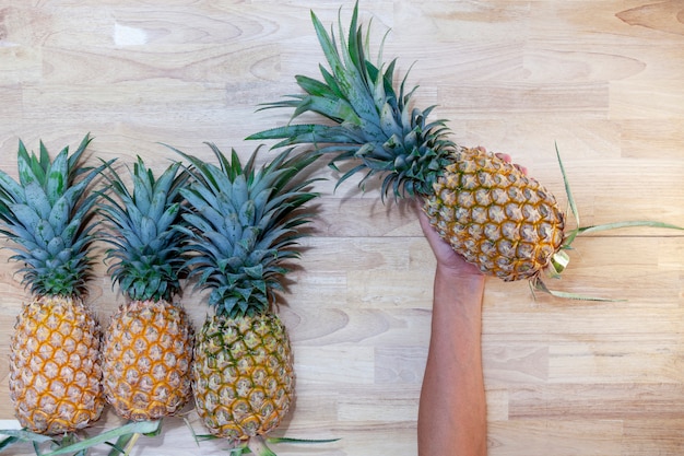 Hand holding pineapple with Row of pineapple fruits on wooden table background