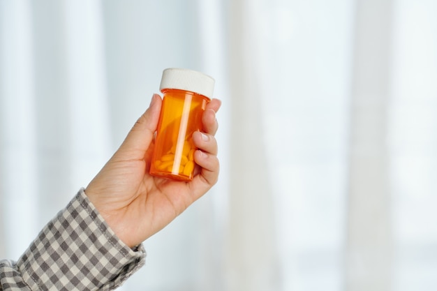 Hand holding plastic jar with pills, supplements or painkillers