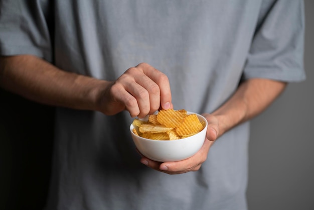 A hand holding potato chips in white bowl