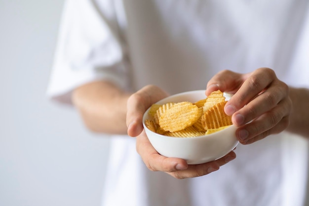 A hand holding potato chips in white bowl