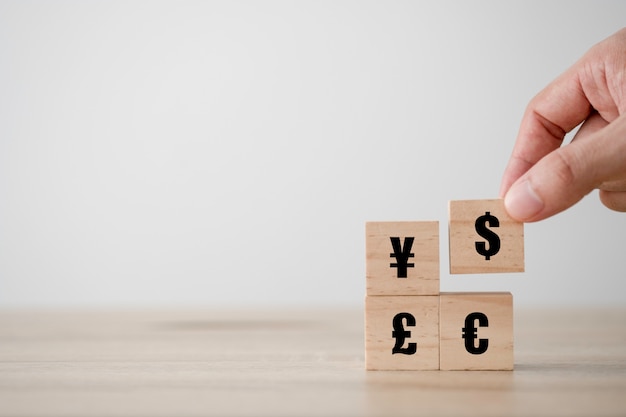 Hand holding and putting US dollar sign is printed screen on wooden cube to Yuan Yen Euro an pound sterling currency. Money exchange and forex concept.