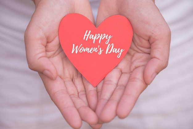 Hand holding red heart paper with Happy Women's Day message concept.