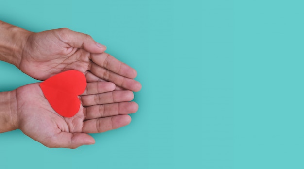 Mano che tiene il cuore rosso su sfondo pastello giornata mondiale del cuore.