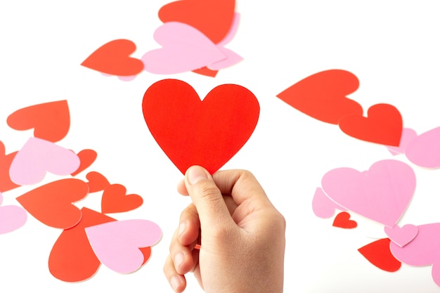 Hand holding a red heart shaped paper craft isolated, red and pink heart shaped paper craft are scattered, concept love and valentine's day.