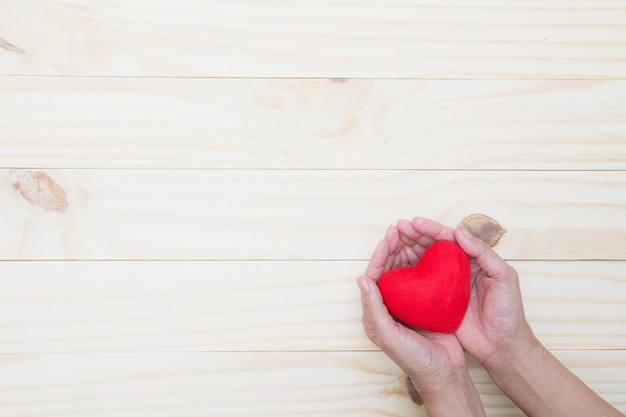バレンタインデーのコンセプトのために木製のテーブルに赤い心臓を保持する手。