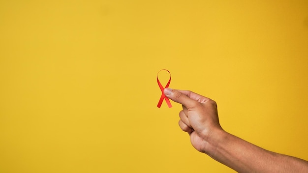 노란색 배경에 빨간색 HIV 리본을 들고 있는 손