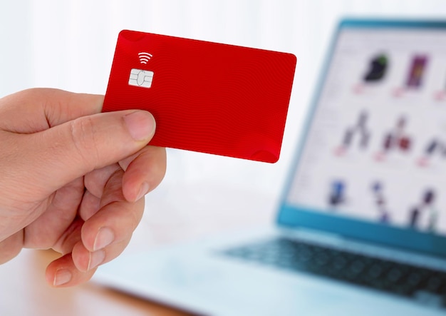 Hand holding a Red plastic credit card and using laptop Online shopping concept