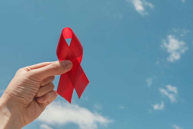 Hand holding red ribbon over blue sky