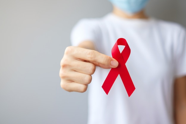 Hand holding Red Ribbon for December World Aids Day (acquired immune deficiency syndrome), multiple myeloma Cancer Awareness month and National Red ribbon week. Healthcare and world cancer day concept