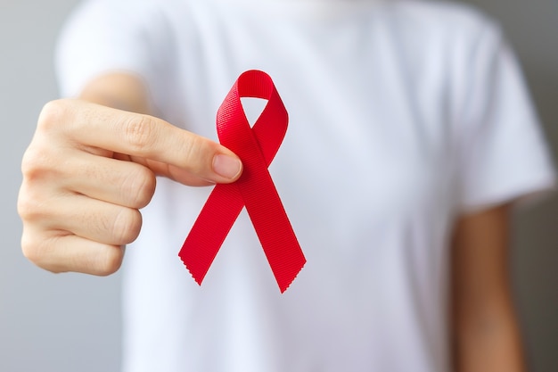 Hand holding Red Ribbon for December World Aids Day (acquired immune deficiency syndrome), multiple myeloma Cancer Awareness month and National Red ribbon week. Healthcare and world cancer day concept