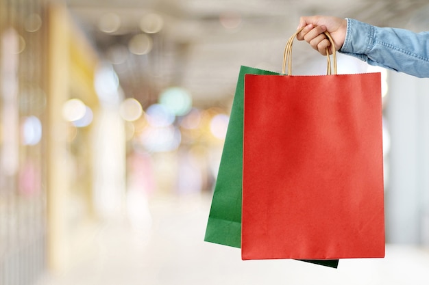 Hand holding red shopping bag on blur store background, banner with copy space for text, template, business concept