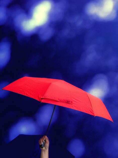 Photo hand holding red umbrella against dark blue wall