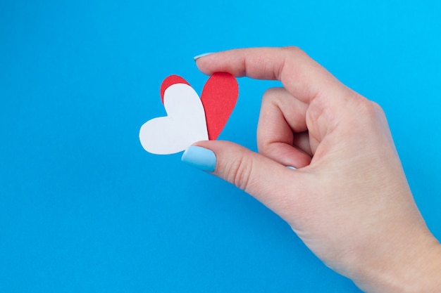 Photo hand holding a red and white heart on a red and blue background. background for valentine's day