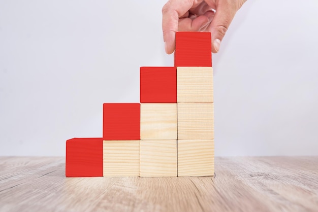 Foto mano che tiene il blocco di legno rosso sul gradino più alto. concetto di percorso di carriera della scala per il processo di successo della crescita aziendale