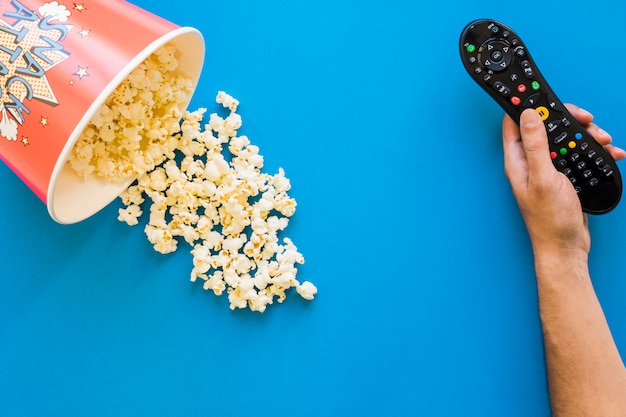 Photo hand holding remote control next to bucket of popcorn