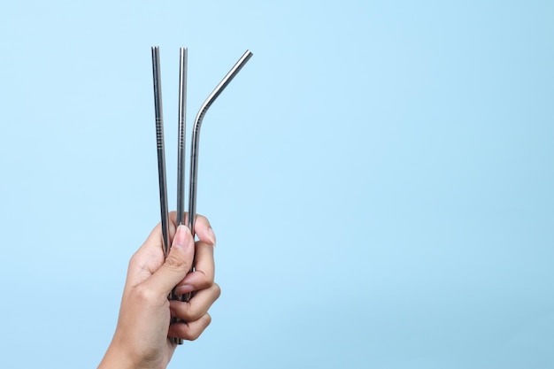Photo hand holding reusable stainless steel straws on blue background eco friendly concept