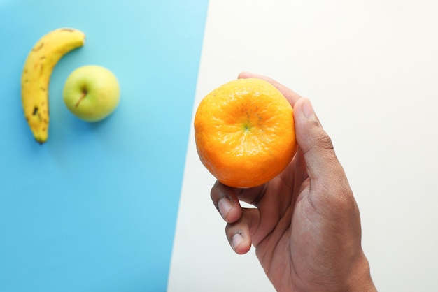 Hand holding ripe orange fruit on color background