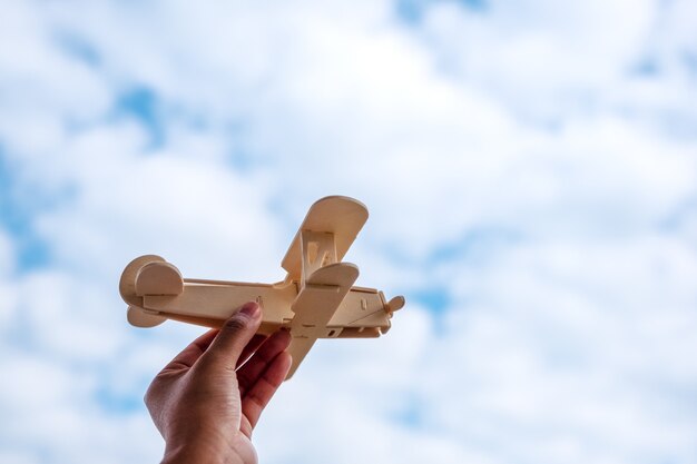 青い空の背景に木製の飛行機を持って上昇する手