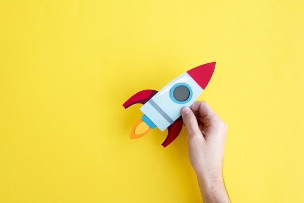 Hand Holding Rocket Spaceship on Yellow Background