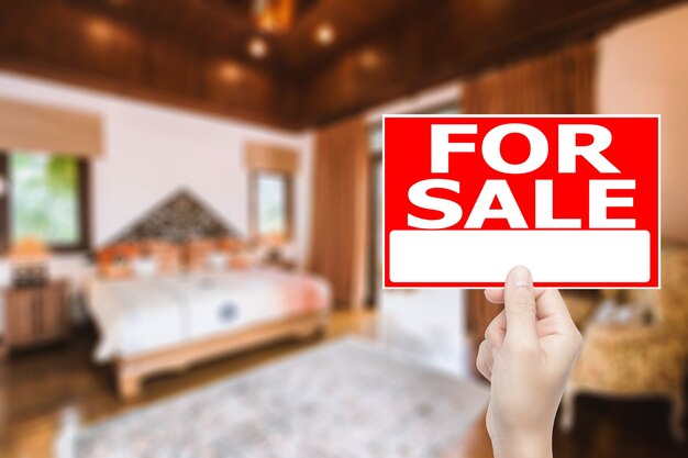 Photo hand holding for sale house sign with house interior background