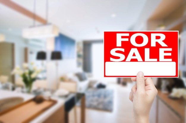 Рука на продажу дом знак с фоном интерьера дома