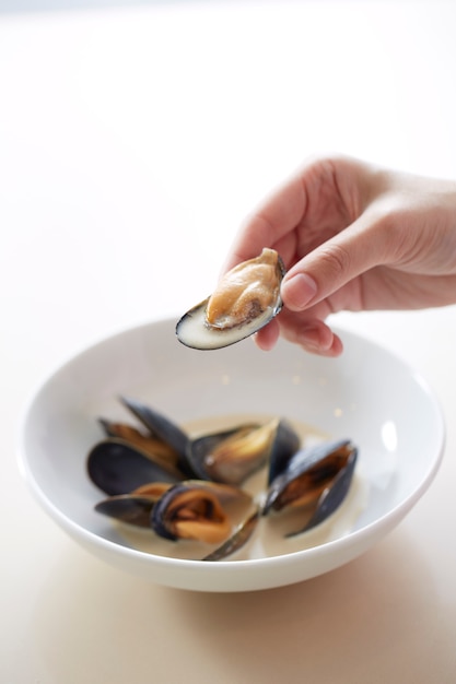 Hand holding scallop shell with scallop meat and soup inside