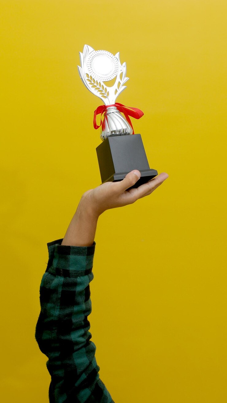 Фотография в руке серебряный трофей чемпиона на желтом фоне