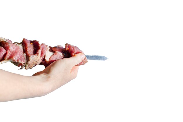 Hand holding a skewer of raw meat on an isolated background
